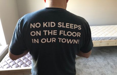Man from Sleep in Heavenly Peace assembling a bed, wearing a shirt that says, "NO KID SLEEPS ON THE FLOOR IN OUR TOWN!"